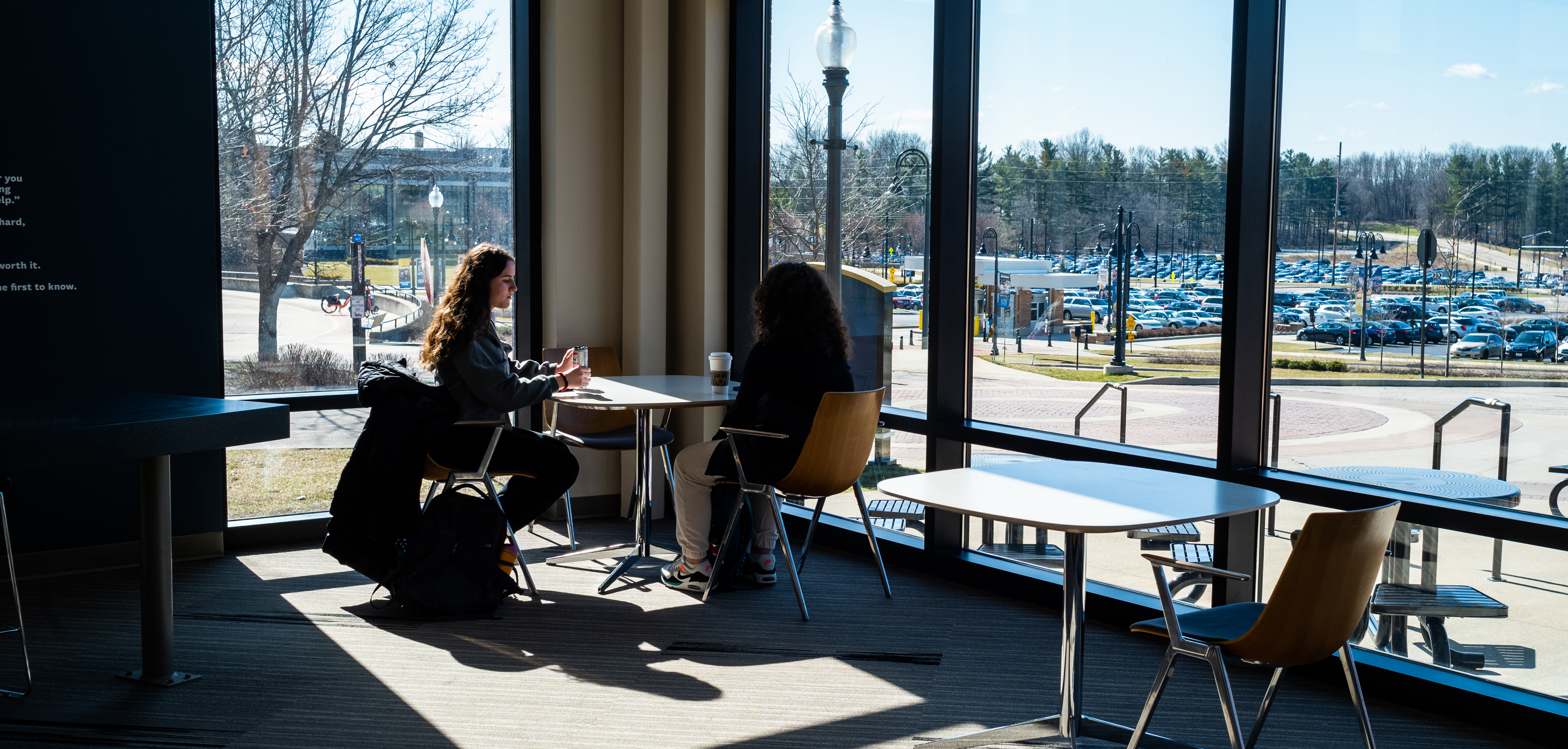 Two students sit inside at a table on a sunny day at Kent State University