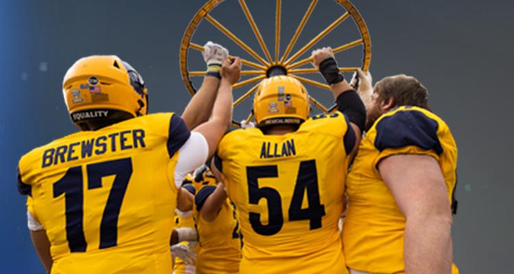 Group of Golden Flashes football players holding up a wagon wheel. Text that reads Saturday October 22