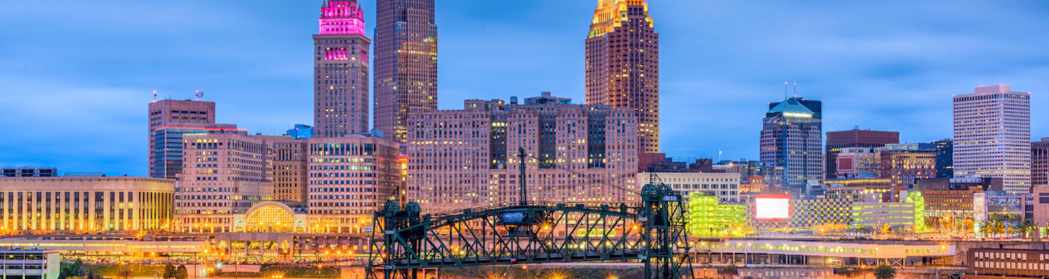 The Cleveland skyline at twilight with Terminal Tower glowing pink, as seen from the Scranton Flats, with the Cuyahoga River and Eagle Avenue Bridge in the foreground.