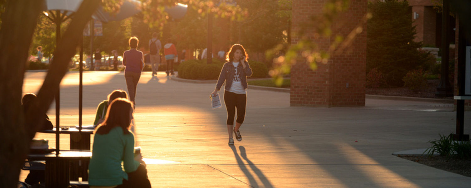 A student walks through the Risman Plaza on a warm fall evening.