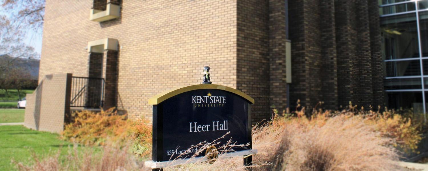 Squirrel eating a paper pie stands on top of the Heer Hall sign at Kent State University.